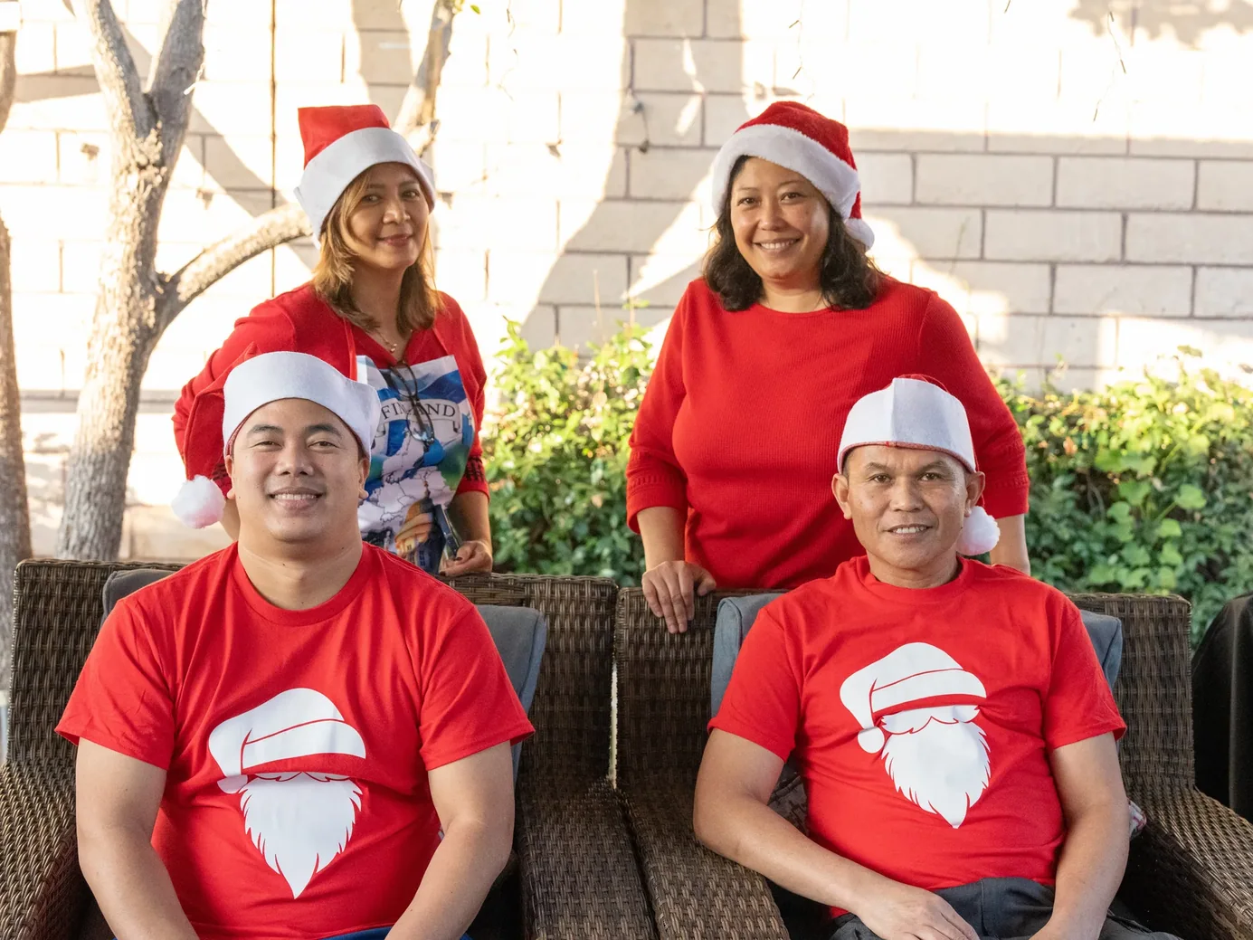 Four smiling individuals in festive red Santa shirts celebrating outdoors
